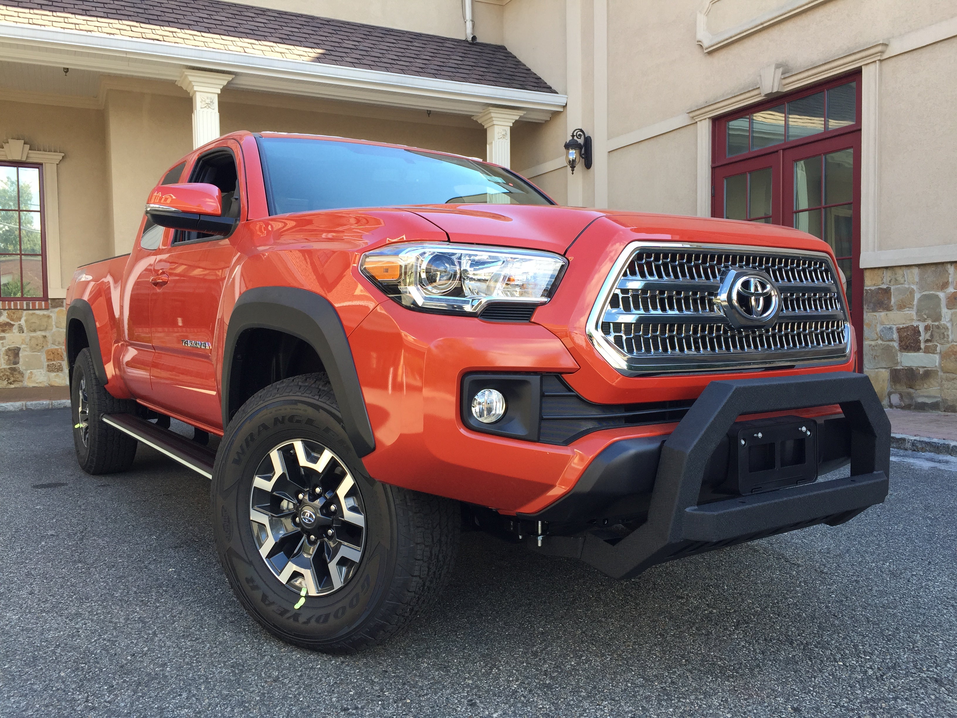 Red Toyota Tacoma with Exterior Parts and Off-Road Accessories. Front Bull Bar Bumper Guard installed in the front of the Toyota Tacoma. Broadfeet Running Boards installed on the passenger side of the Toyota Tacoma.